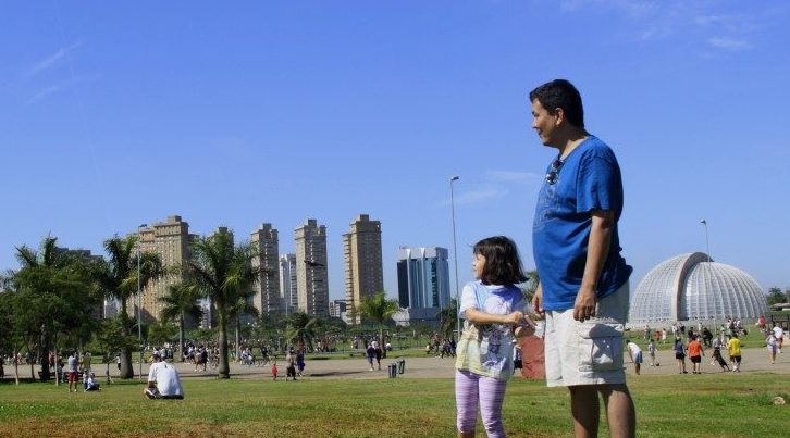 Criança observa com pai uma pipa voando sobre parque
